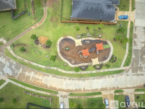 A playground with a slide, swings, and a sandbox is surrounded by a grassy area.