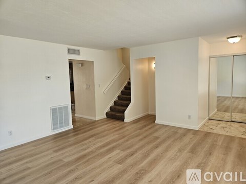 A spacious room with wooden flooring and a staircase leading to another level.