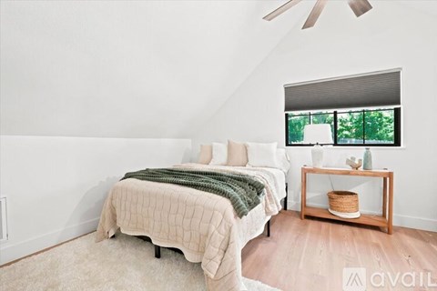 A bedroom with a bed, a fan, and a window with a view of trees.