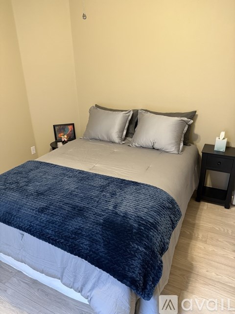 A bed with a blue blanket and two pillows sits in a room with a wooden floor.