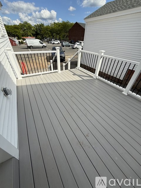 A wooden deck with a white railing and a view of a parking lot and trees.