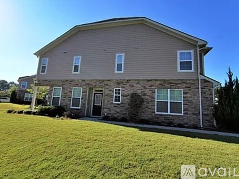A house with a brown siding and a stone foundation is surrounded by a green lawn.