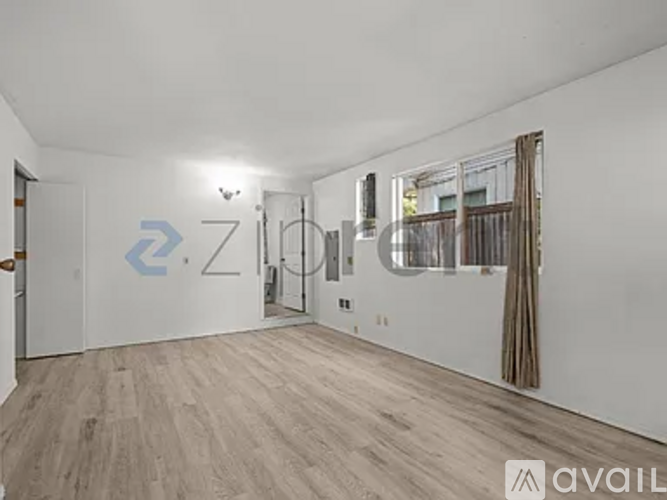 A spacious room with wooden flooring and a large window with curtains.