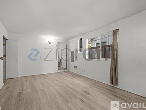 A spacious room with wooden flooring and a large window with curtains.