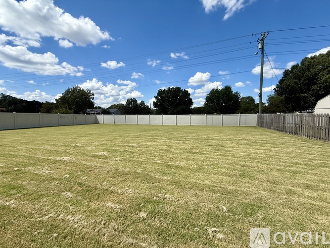A large, open grassy field with a fence and trees in the distance.