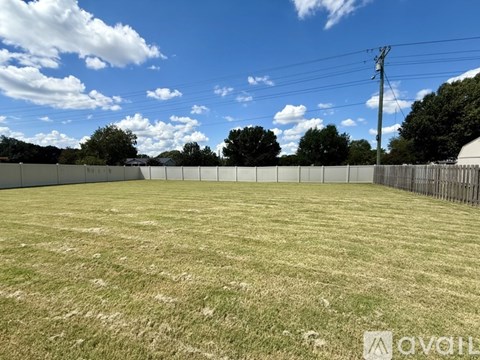 A large, open grassy field with a fence and trees in the distance.