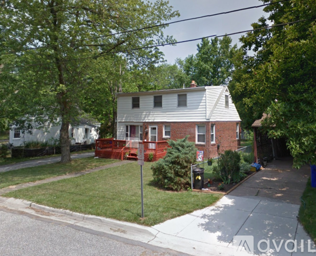 A house with a red brick exterior and a white trim is surrounded by trees and has a lawn in front.