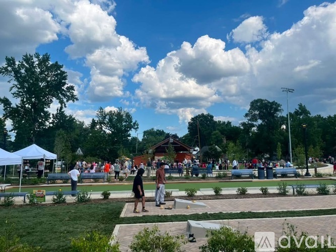 A group of people are gathered in a park with a white tent and a playground.