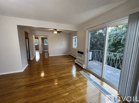 A spacious room with wooden flooring and a sliding glass door leading to a balcony.
