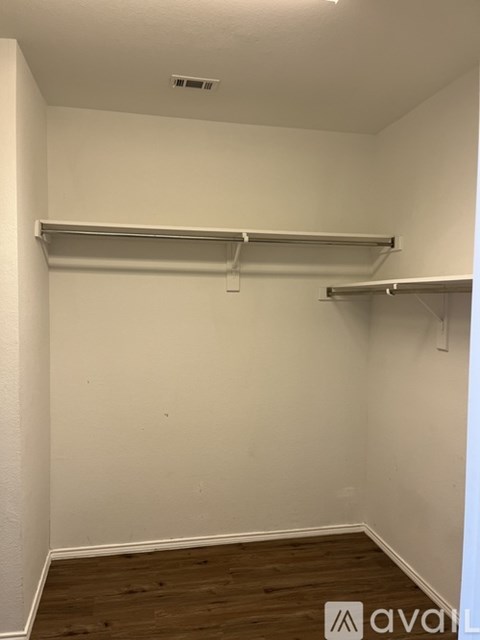 A room with white walls and wooden flooring with two metal shelves.