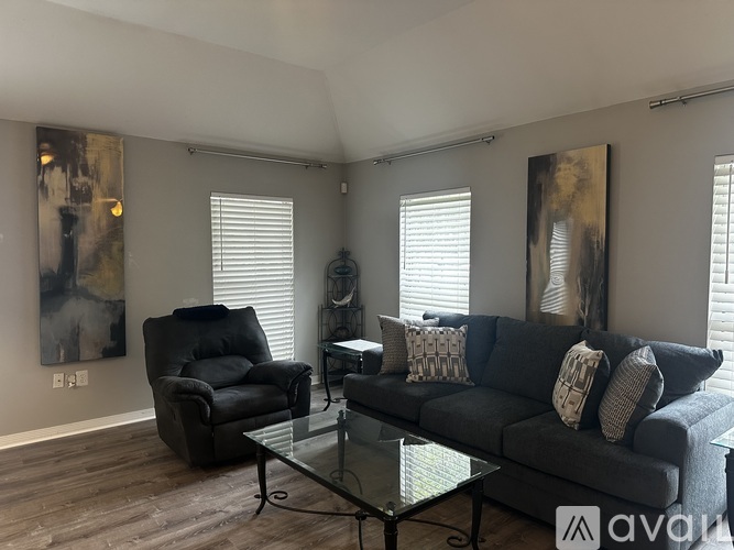 A living room with a black couch, a black chair, and a glass coffee table.