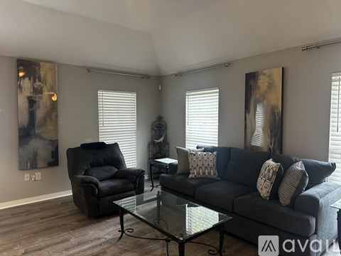 A living room with a black couch, a black chair, and a glass coffee table.
