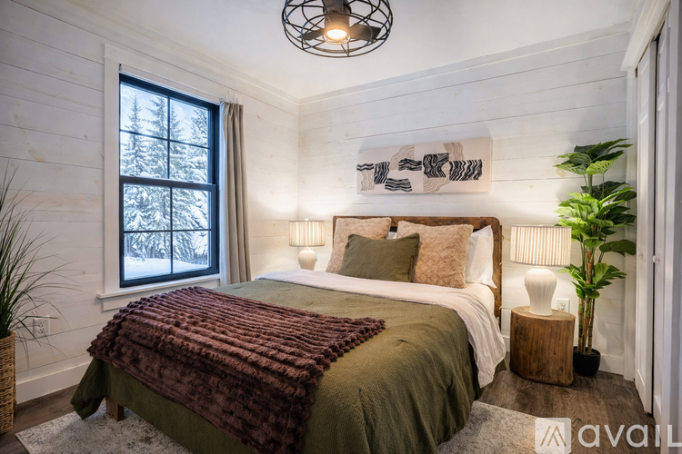 A bedroom with a bed covered in a green blanket and a window showing a snowy scene outside.