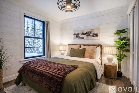 A bedroom with a bed covered in a green blanket and a window showing a snowy scene outside.