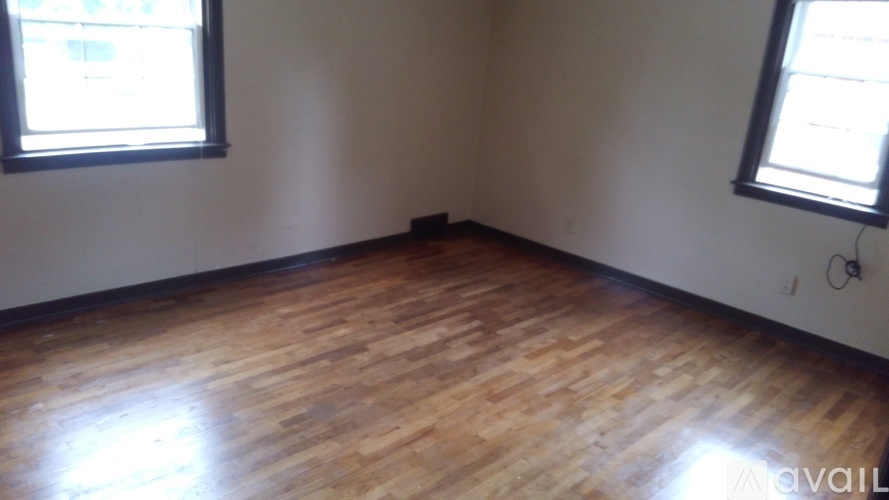 A room with wooden flooring and two windows.