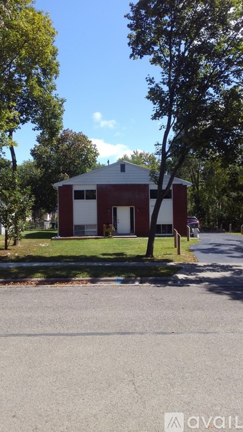 A small red building with a white roof is situated on a grassy area with a tree in front of it.