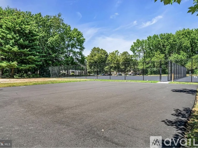A large, empty parking lot surrounded by a fence and trees.