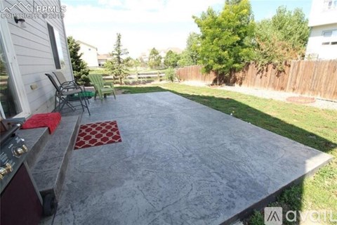 A backyard with a concrete patio and a grill.