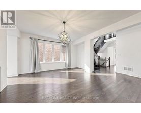 A spacious room with wooden flooring and a staircase in the background.