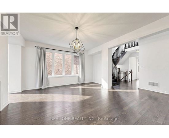A spacious room with wooden flooring and a staircase in the background.