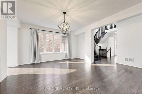 A spacious room with wooden flooring and a staircase in the background.