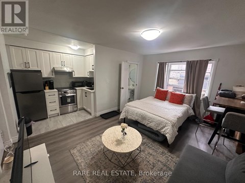 A bedroom with a bed, a table, and a kitchen area.