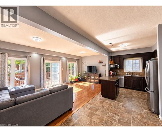 A well-lit, spacious kitchen and living room with a grey sofa and wooden floors.