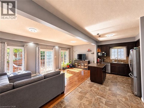 A well-lit, spacious kitchen and living room with a grey sofa and wooden floors.