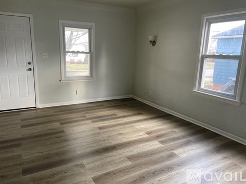 A room with wooden flooring and two windows.