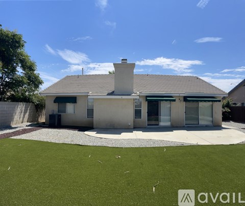 A house with a grey roof and a chimney is surrounded by a gravel driveway and a grassy area.
