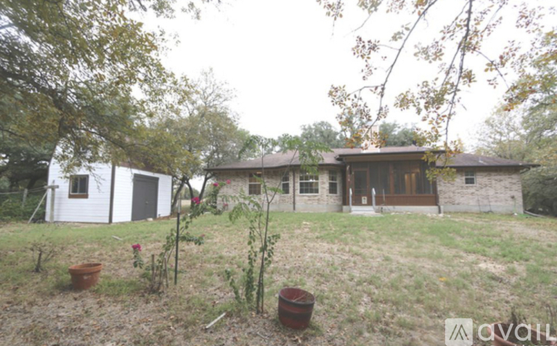 A house with a white exterior and a brown roof is surrounded by trees and has a small garden in front.