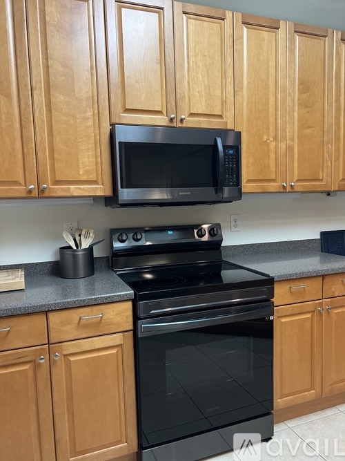 A black microwave oven is on top of a black stove in a kitchen with wooden cabinets.