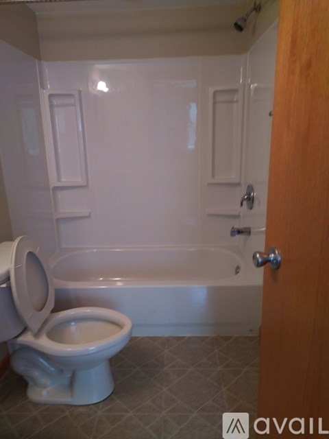A white toilet is in a bathroom with a bathtub and a door.