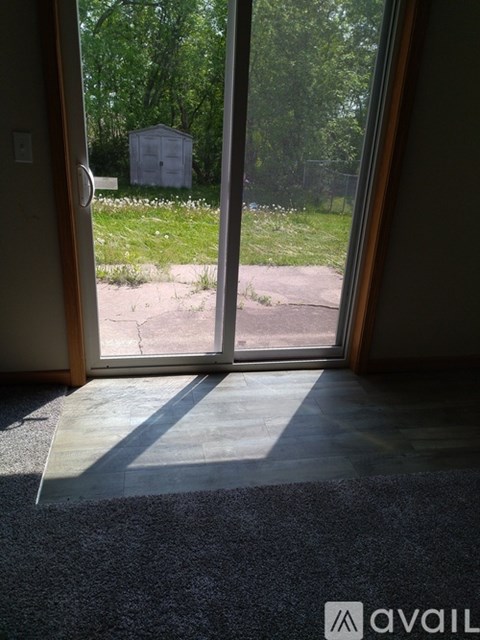 A room with a carpeted floor and a view of a grassy area through a glass door.