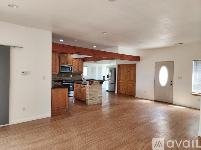 A spacious living room with wooden floors and a kitchen area in the background.