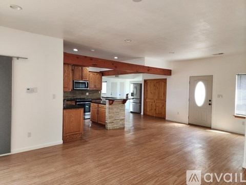 A spacious living room with wooden floors and a kitchen area in the background.