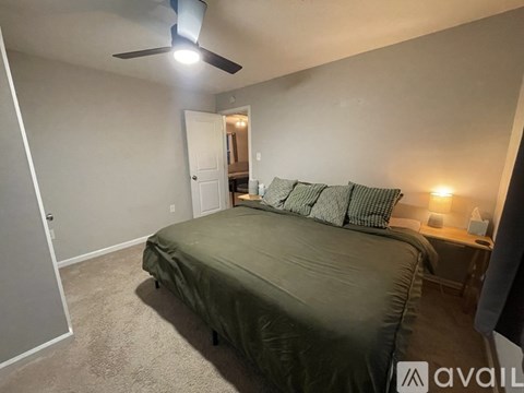 A bedroom with a bed, a ceiling fan, and a nightstand with a lamp.