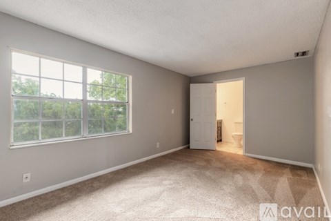 A room with a carpeted floor, a window with a view of trees, and a door leading to another room.