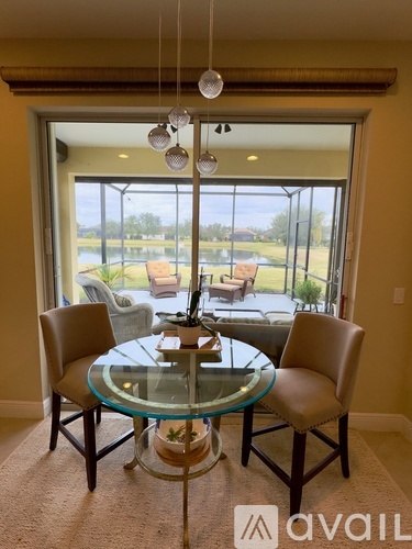 A glass dining table with four chairs is set in a room with a view of a lawn and trees outside.