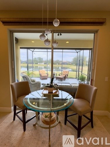 A glass dining table with four chairs is set in a room with a view of a lawn and trees outside.