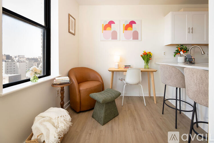 A living room with a brown leather chair, a white chair, a green ottoman, and a table with a vase of flowers and a lit candle.