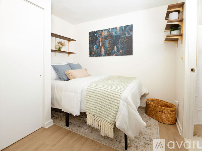 A bedroom with a bed covered in a white blanket and a painting on the wall.