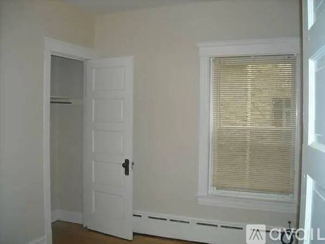 A white door with a black handle is on the left and a window with blinds is on the right.
