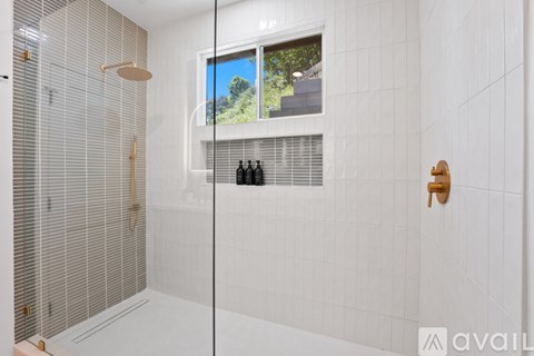 A bathroom with a glass shower door and a window showing a view of trees.