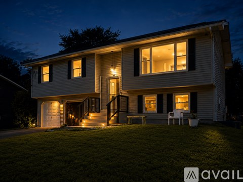 A house with a lit up front porch and a sign that says "AVAIL" in the front yard.