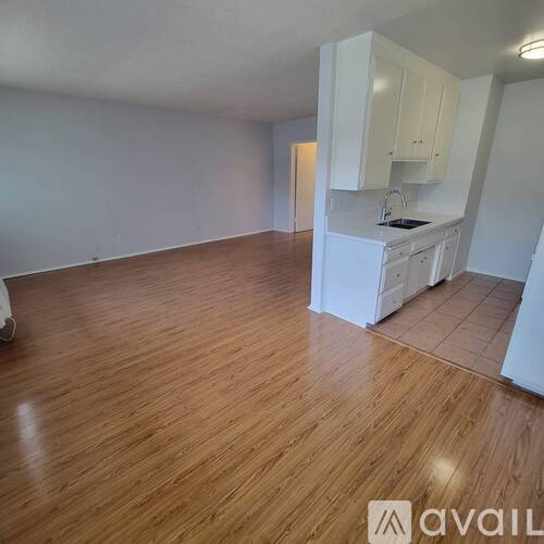 A kitchen area with wooden flooring and white cabinets.