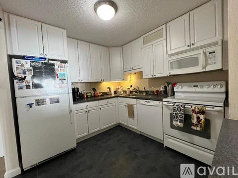 A kitchen with white cabinets and appliances, a refrigerator on the left, and a microwave above the stove.