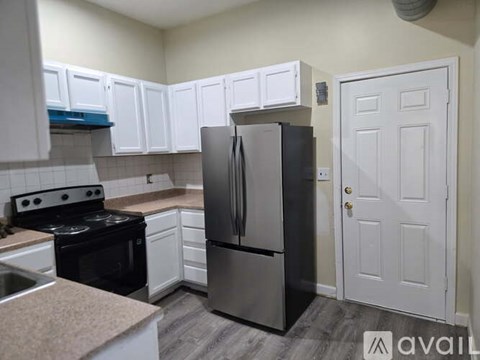 A kitchen with a black refrigerator, white cabinets, and a white door.