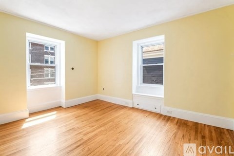 A room with wooden floors and two windows, one of which has a view of a building outside.