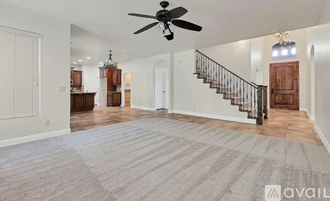 A spacious living room with a staircase and a ceiling fan.